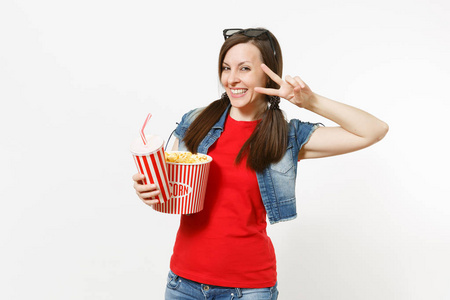 在3d 眼镜的年轻微笑的女人的肖像看电影, 拿着一桶爆米花和塑料杯苏打或可乐显示的胜利标志孤立的白色背景。情感在戏院