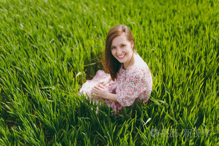 微笑美丽的女人穿着浅色图案的衣服坐在草地上放松休息在阳光明媚的