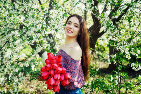 春天公园的年轻女子。女孩在盛开的花园里捧着红色的郁金香