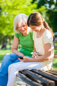 祖母和孙女坐在公园里, 用手机