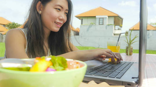 年轻美丽和快乐的亚洲华人妇女在户外工作与膝上型电脑网络绿草背景咖啡馆在数字游牧和互联网自由职业者的工作概念