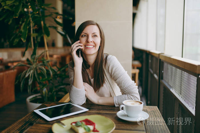 快乐的女人坐在咖啡馆里, 喝着卡布奇诺, 蛋糕, 在手机上聊天, 在餐厅休息的时候放松。女性在电脑平板电脑上工作, 在咖啡馆休息