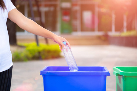 妇女手捧和把塑料瓶废料放进垃圾桶里照片