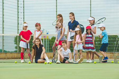 一组女孩作为网球运动员举行网球拍反对户外球场绿草的肖像