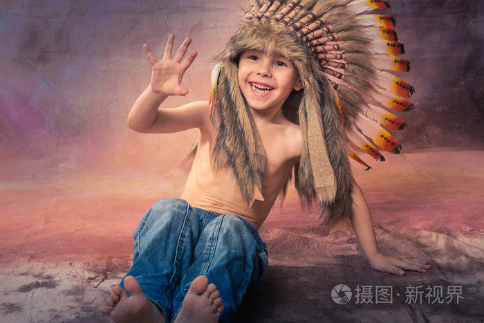 一个小英俊的男孩大声笑瀑布坐在美国印第安人羽毛的皇冠