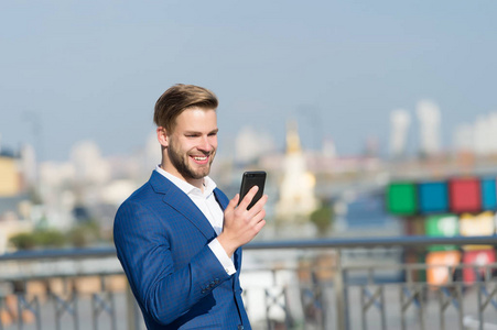 商人快乐的微笑使用智能手机视频通话或短信, 天际线背景。业务呼叫概念。男士西装商人利用现代移动技术为企业带来优势