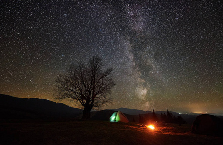 动感之星网站明亮的篝火在两个旅游帐篷之间燃烧, 黑暗, 从里面点燃.