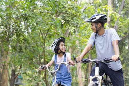 快乐的父亲和女儿骑自行车在公园里