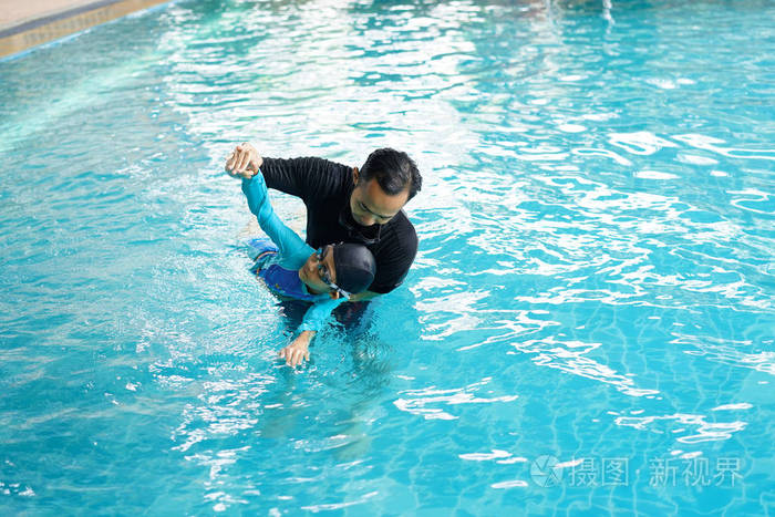 父亲教女儿在游泳池游泳