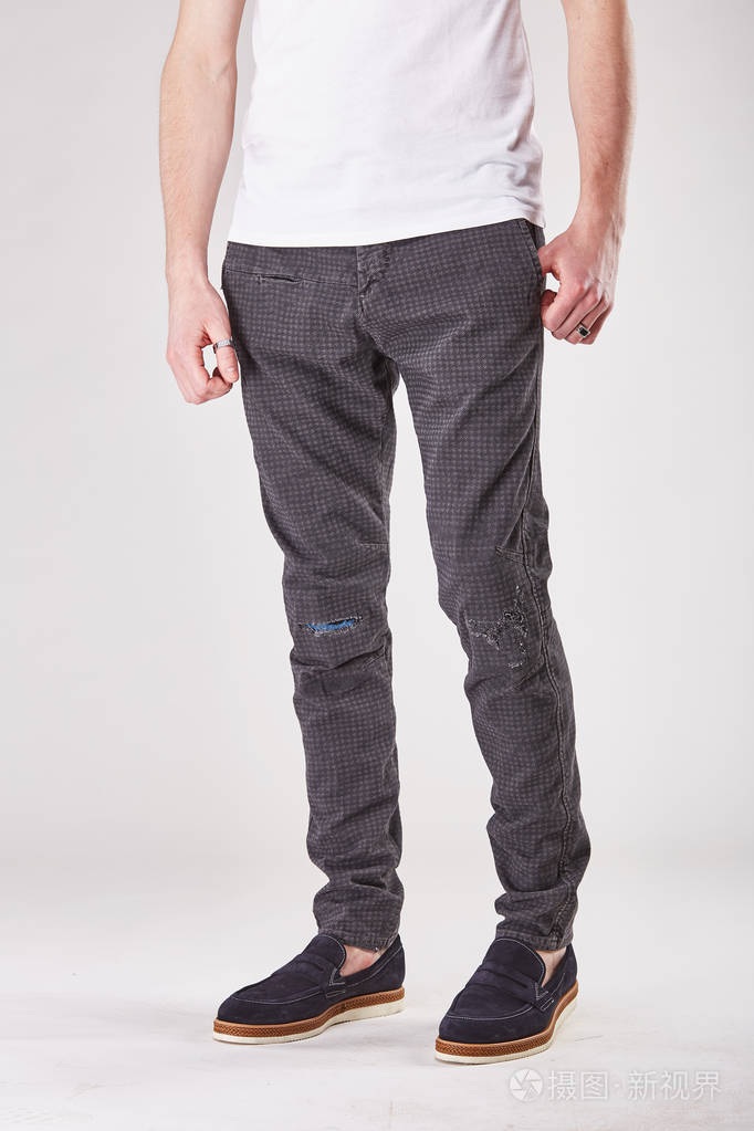 男人正站在时尚的灰色和棕色斜纹棉布裤和黑色的鞋子光摄影棚里