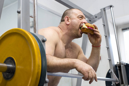 男人吃肉和奶酪汉堡包在健身房里