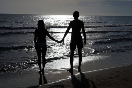 浪漫的情侣牵着手在日落时分在沙滩上