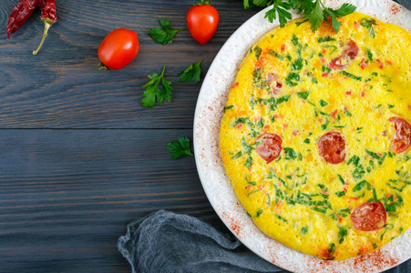 煎蛋饼.意大利煎蛋卷与奶酪, 绿色和西红柿在一个白色的盘子上的木质背景。顶部视图