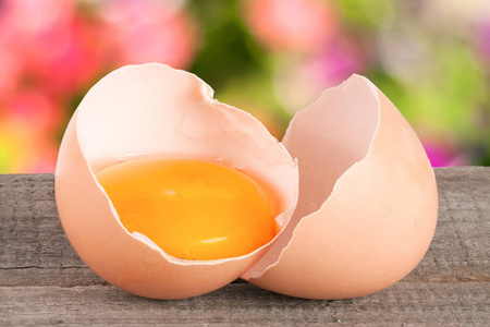 破的蛋的蛋黄和蛋壳与模糊的花园背景木制的桌子上