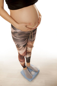 怀孕妇女站在体重秤上白色背景