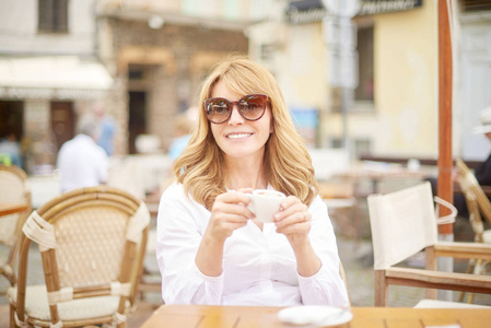 坐在户外咖啡馆享受她的浓咖啡的快乐中年妇女肖像
