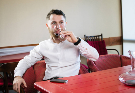 有吸引力的年轻男子坐在桌前和从玻璃在餐厅喝葡萄酒