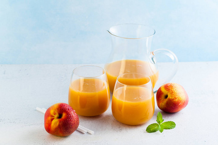 桃汁在玻璃和一个滗水器和新鲜桃子与叶子在桌上。蓝色背景。复制空间