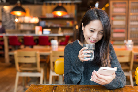 女人看着手机，喝杯水