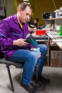 一个穿着牛仔裤的年轻人在缝纫车间用特制的吹风机做鞋底的儿童鞋。