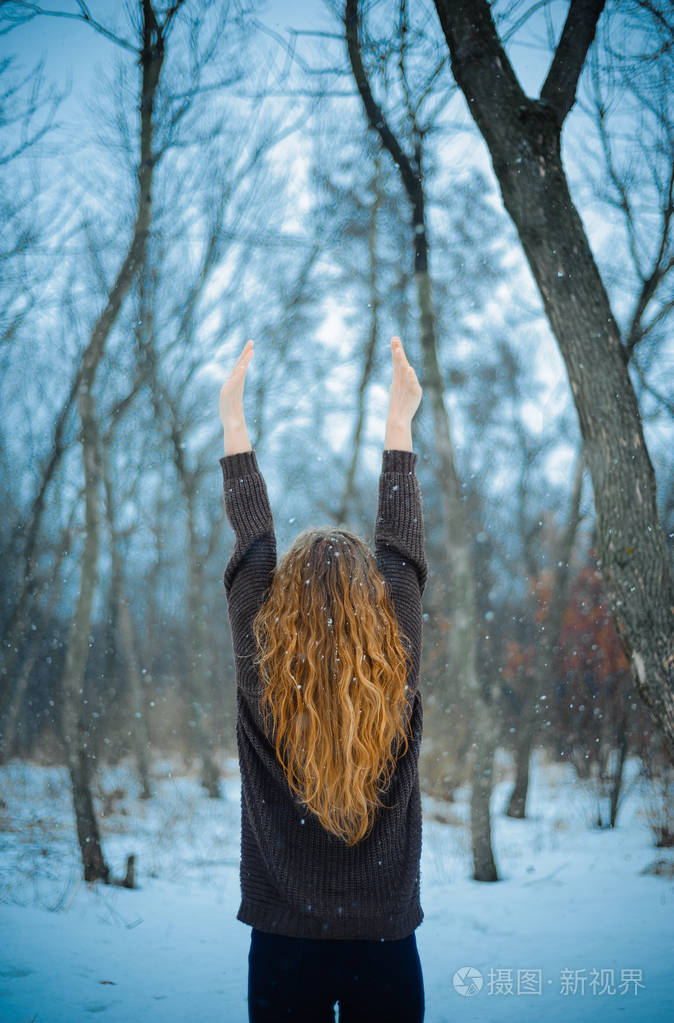欧洲人的年轻女孩与红色的头发和蓝色的眼睛在自然公园里冬天走在雪上