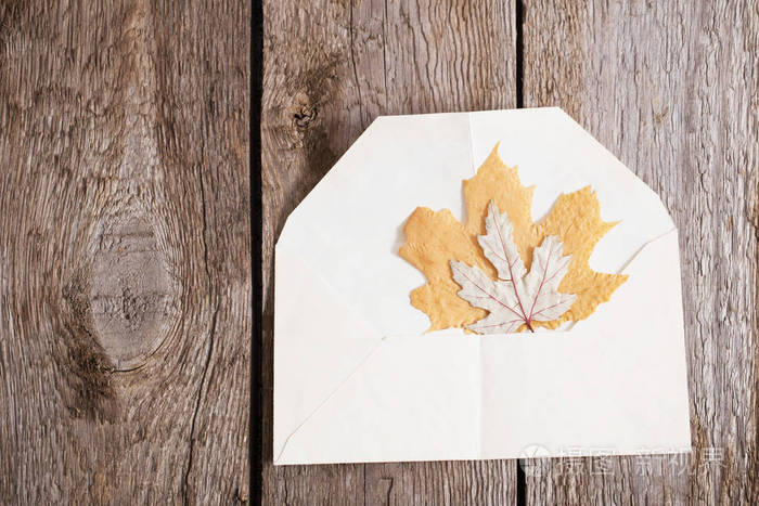 在木质背景的信封上的秋天叶子