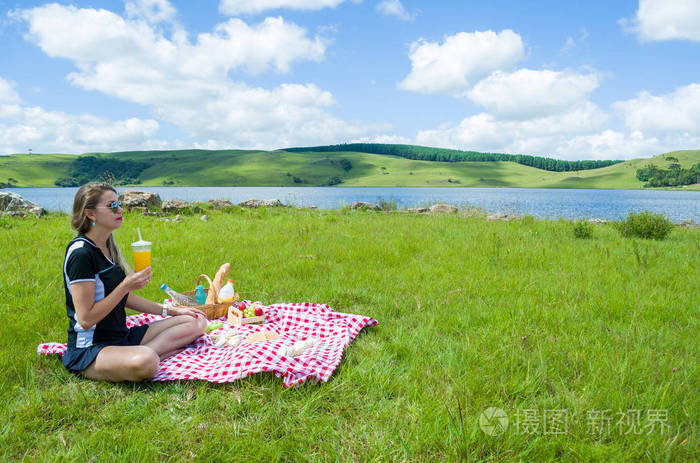 在绿色草坪上做野餐的年轻妇女以美丽的风景