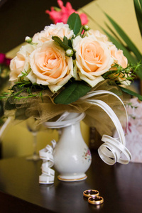 婚礼新娘捧花的橙色玫瑰用木制的桌子上的结婚戒指特写