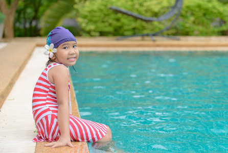 快乐的小女孩微笑着, 穿着游泳帽坐在室外游泳池的夏天。生活方式和娱乐概念