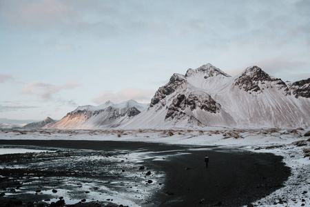 一个人站在黑色沙滩上的积雪覆盖的景观在 Stokksnes, 冰岛