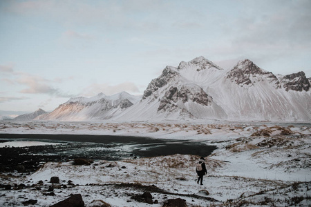 一个人走过积雪覆盖的领域对 Stokksnes, 冰岛的黑色沙滩