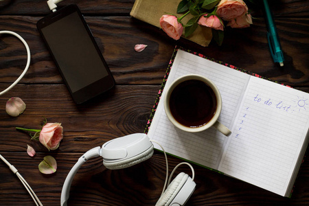 做列表概念。一张木桌上的智能手机耳机咖啡杯和笔记本。顶部视图平面放置背景