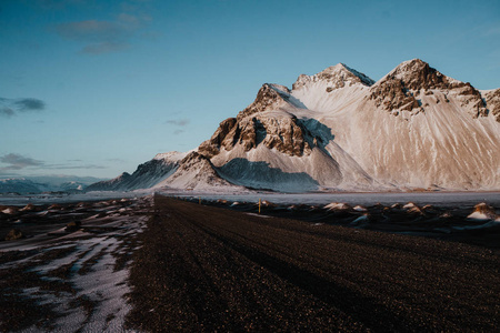 在 Stokksnes, 冰岛在日落的雪域旁边的泥土路