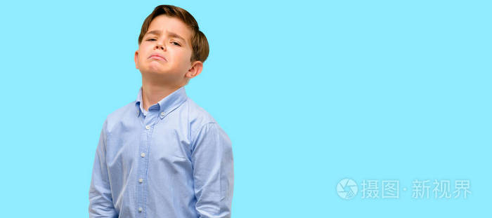 英俊的蹒跚学步的孩子与绿色的眼睛悲伤和不安的表情不高兴的蓝色背景