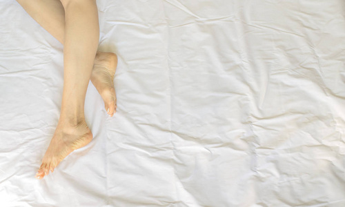 女性腿在床视图从上面, 白色床上用品