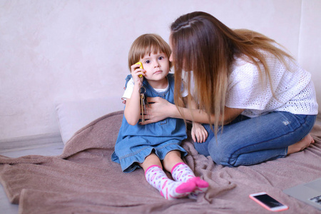 年轻母亲坐在小女儿和智能手机上的床上