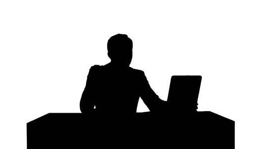 剪影愉快的商人坐在办公室用手提电脑和说在照相机照片