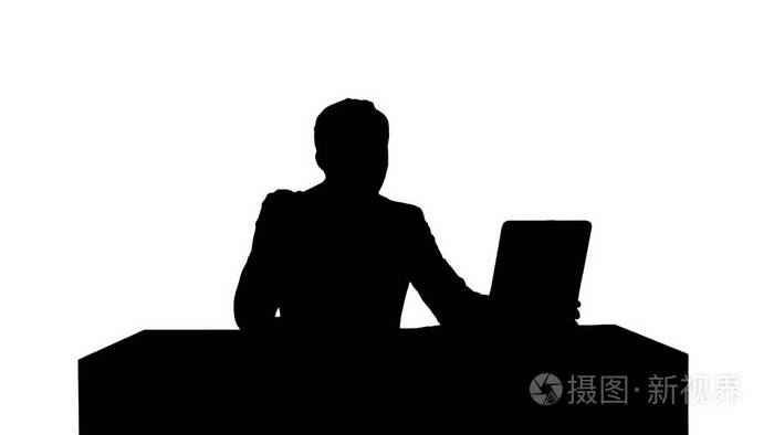 剪影愉快的商人坐在办公室用手提电脑和说在照相机