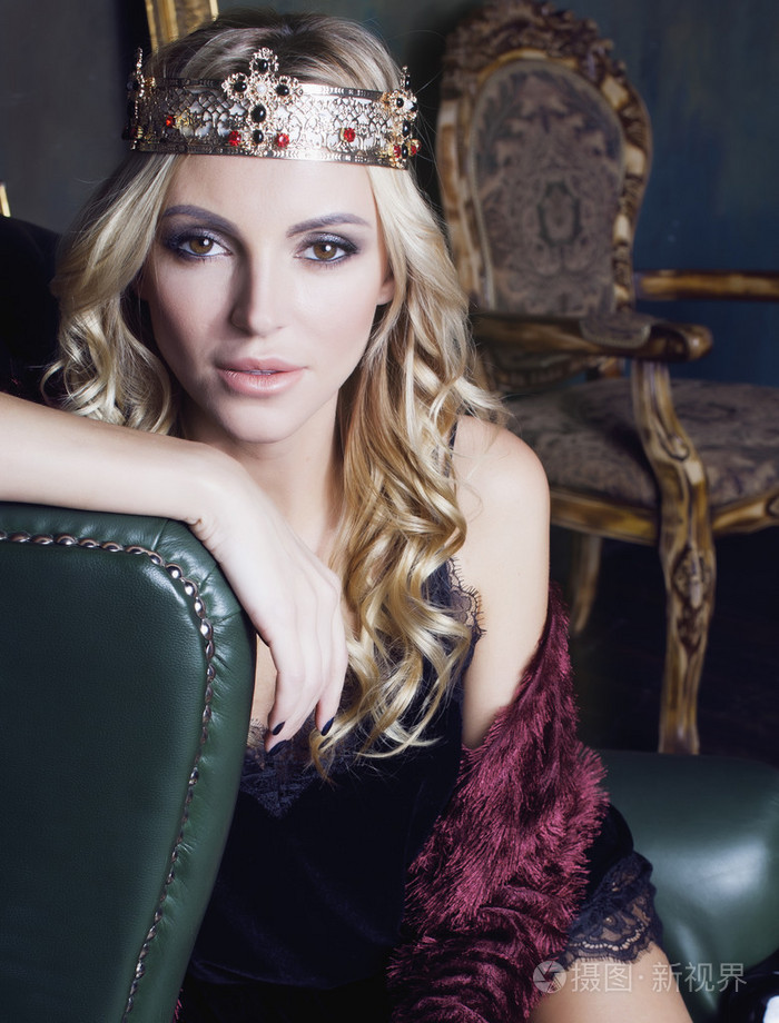 年轻的金发美女戴王冠在童话豪华的内饰,古色古香的空框架总财富