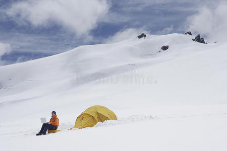 雪山坡帐篷边用笔记本的徒步旅行者