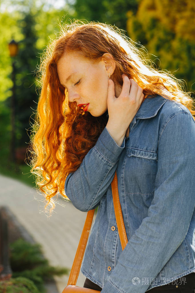 可怕的红发女孩在蓝色牛仔衬衫摆在阳光下的公园