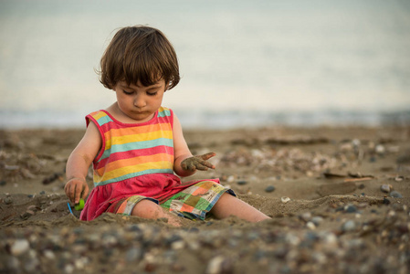 可爱的蹒跚学步婴儿在鹅卵石海滩上玩