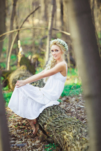 美丽的妇女穿着白色礼服坐在树绿色森林