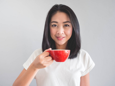 微笑亚洲妇女喝咖啡从红色杯子