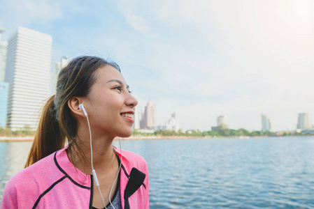 年轻的亚洲妇女放松自己通过听音乐后, 城市运行的运动与城市的视野背景和温暖的光清除天空的下午晚些时候。户外跑步运动概念