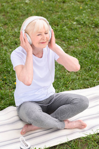 坐在瑜伽垫上的资深妇女听音乐与耳机