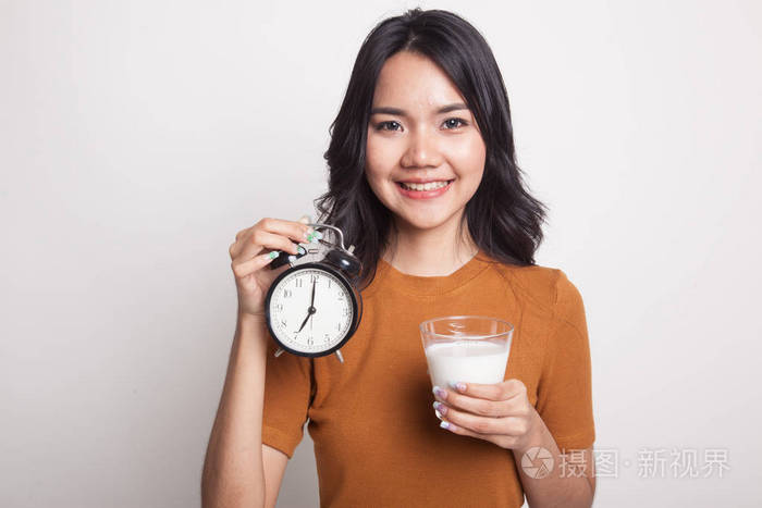 健康的亚洲女人喝杯牛奶举行时钟