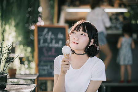 亚洲女孩的肖像白色衬衫和裙子吃冰淇淋在户外自然复古电影风格