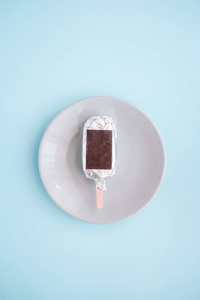 冰淇淋, 冰棒包裹在银铝箔从上面的圆板。柔和的蓝色背景。简约食品摄影。Copyspace