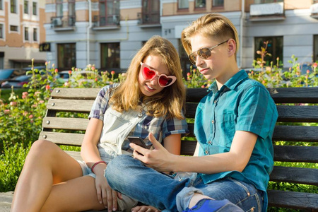 十几岁的朋友女孩和男孩坐在城市的长凳上, 说话。友谊与人的理念